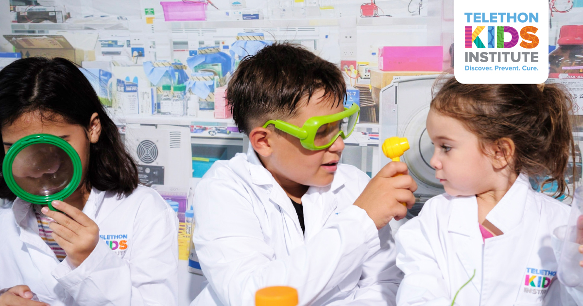 3 children dressed up in The Kids lab kits interacting with various scientific instruments